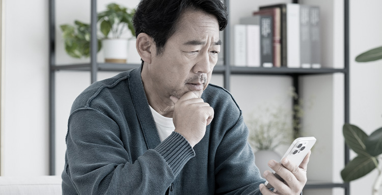 スマートフォンを見ながら悩む男性